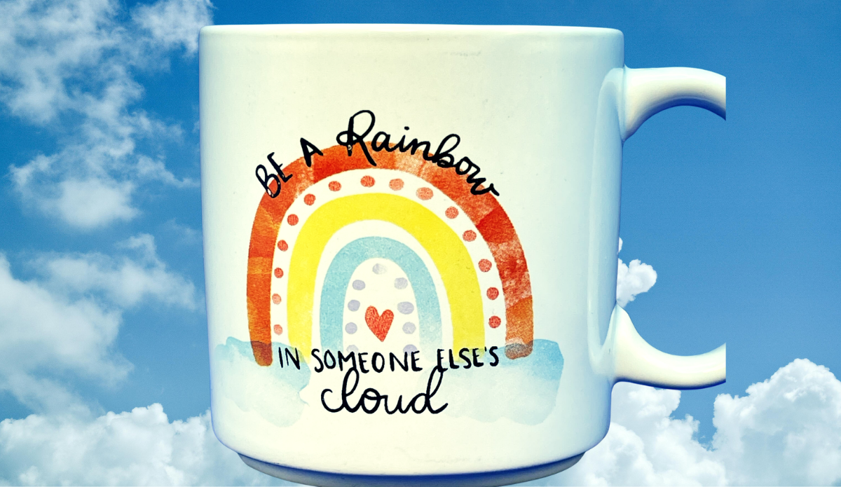 Be A Rainbow Inspirational Mug against blue sky and clouds with colorful rainbow artwork and uplifting message