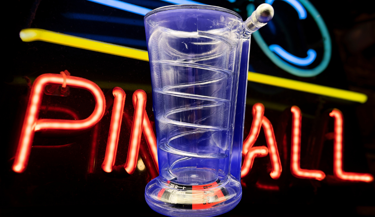 Pinball Pint Glass Drinking Game displayed in front of a colorful neon pinball sign