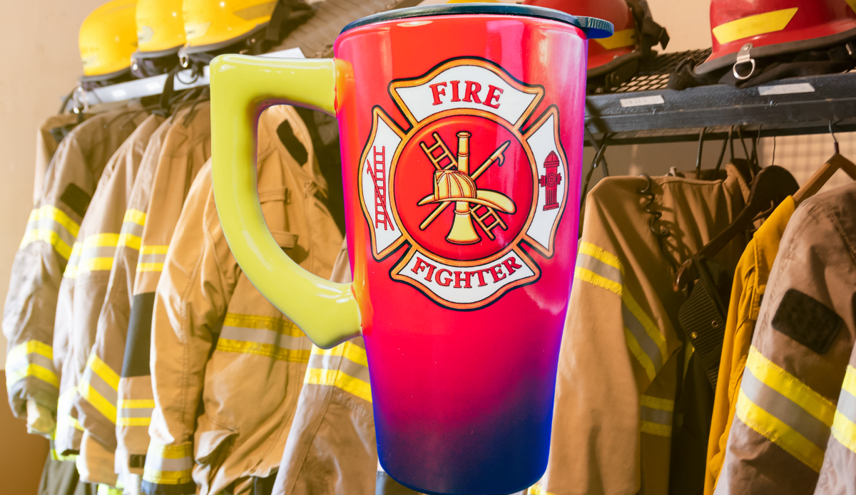 Firefighter Maltese Cross Travel Mug in firehouse scene with firefighter gear, red and navy body, yellow handle, and emblem