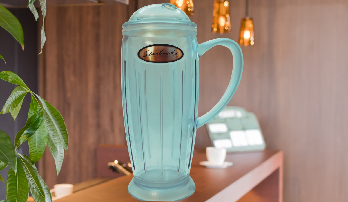 2001 Starbucks Rocket Tumbler displayed in a warm café setting with greenery and hanging lights