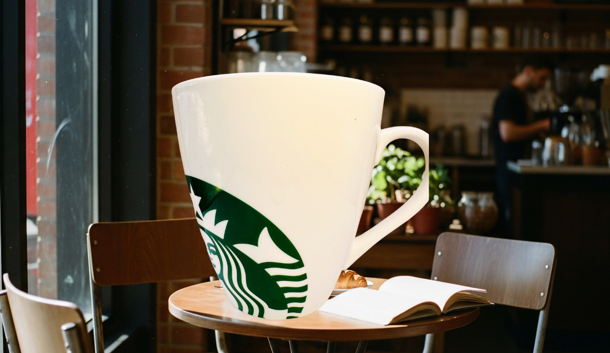 Starbucks White Giant Siren Mug displayed in a warm café with an open book