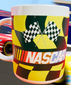 NASCAR Checkered Flag Logo Mug displayed beside a racetrack with stock cars racing in the background.