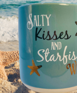 Salty Kisses Starfish Wishes Mug displayed on beach beside starfish with ocean waves