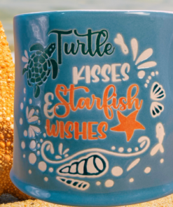 Turtle Kisses Starfish Wishes Mug displayed on sandy beach beside large starfish and ocean water