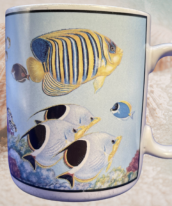 tropical fish mug styled on sandy beach with seashell and ocean water in background