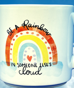 Be A Rainbow Inspirational Mug against blue sky and clouds with colorful rainbow artwork and uplifting message