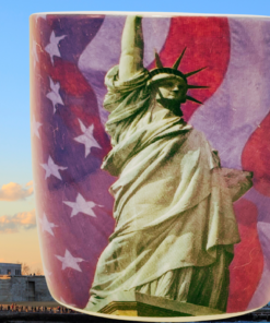 Statue of Liberty Patriotic Coffee Mug displayed with the Statue of Liberty and New York Harbor in the background.