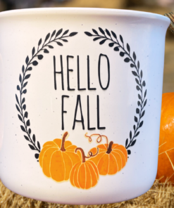 Cynthia Rowley Pumpkin Mug displayed beside an orange pumpkin on hay in an outdoor fall setting