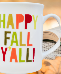 Happy Fall Y'all Mug displayed with autumn leaves, cozy knit texture, and an open book