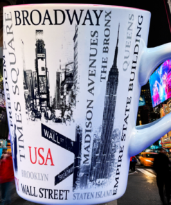 New York City Landmarks Mug displayed amid the bright billboards, traffic, and nighttime energy of Times Square