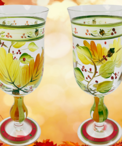Autumn Leaves Wine Glass shown from two sides with hand-painted fall foliage against a glowing autumn leaf background