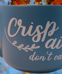 Crisp Air Don't Care Mug displayed with colorful autumn leaves against a bright blue sky