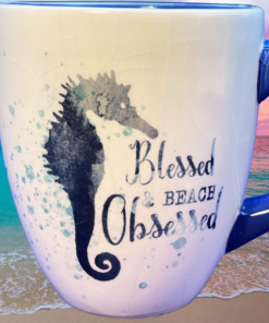 Blessed Beach Obsessed Seahorse Mug displayed against turquoise ocean water and colorful beach sunset