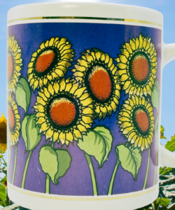 Vintage 1995 Sunflower Coffee Mug displayed in a sunflower field with yellow floral artwork, cobalt blue background, and white handle.