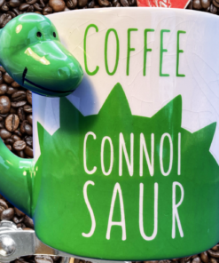 BigMouth Coffee Connoisaur Dinosaur Mug displayed beside a fresh cup of coffee and coffee beans
