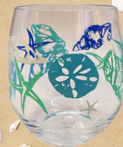 Beach Shells Acrylic Stemless Wine Tumbler displayed on sandy beach with scattered seashells