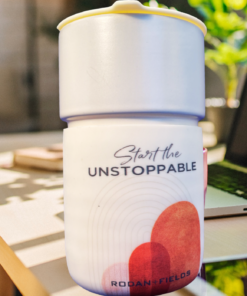 Rodan + Fields Start The Unstoppable Travel Mug on work desk beside laptop in bright motivational workspace