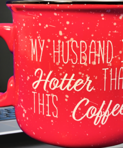 My Husband Is Hotter Than This Coffee Mug displayed on an office desk beside a laptop, pen, and blue notebook