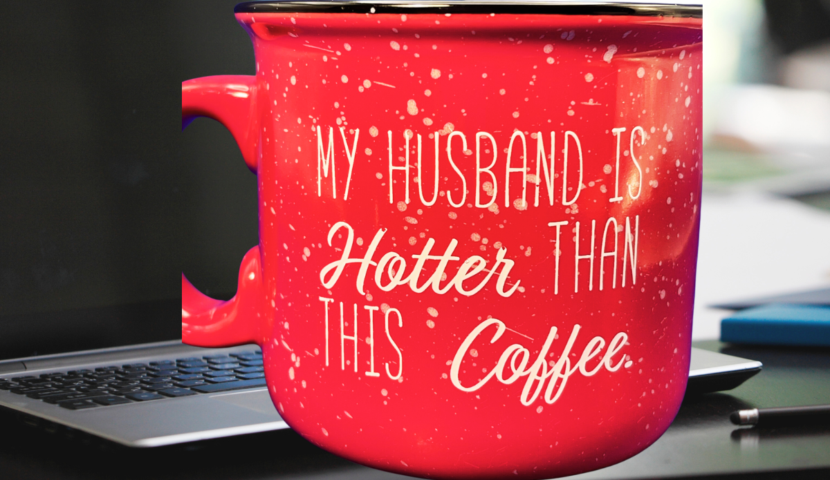 My Husband Is Hotter Than This Coffee Mug displayed on an office desk beside a laptop, pen, and blue notebook