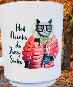 Hot Drinks & Fuzzy Socks Cat Mug displayed in an autumn woodland scene with orange leaves and fall trees