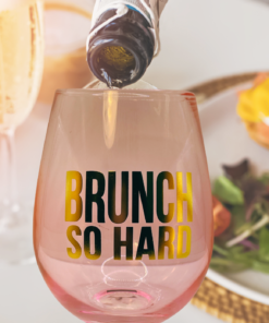 Pink brunch wine glass being filled with champagne next to brunch food and mimosas