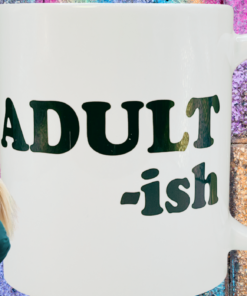 Adultish Funny Coffee Mug in colorful adulting humor scene with glitter brick background and playful model