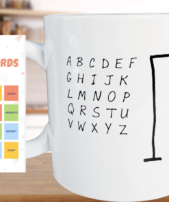 Hangman Game Coffee Mug on a wooden kitchen counter beside a colorful Hardest Hangman Words graphic featuring challenging puzzle words.