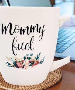 Mommy Fuel floral 20 oz mug on coaster next to laptop on wooden desk