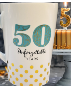Hallmark 50 Unforgettable Years Mug displayed beside a birthday cake topped with glittering gold 50 candles.