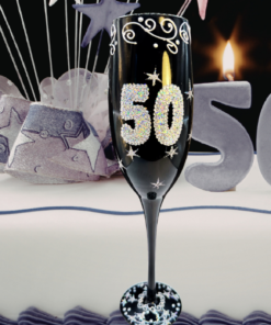 50 Bling Birthday Champagne Flute displayed in front of a white 50th birthday cake with sparkling decorations and lit numeral candles.