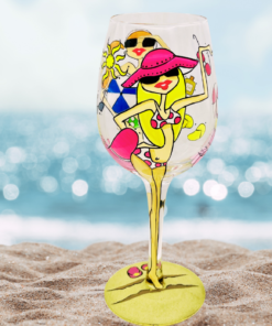 Beach Girls Hand Painted Wine Glass displayed on sand with sparkling ocean water in the background
