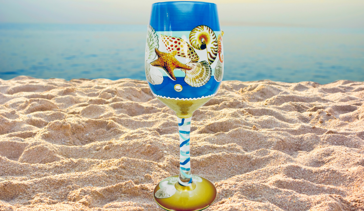 Beach Seahorse Seashell Hand Painted Wine Glass displayed on a sandy beach with ocean waves