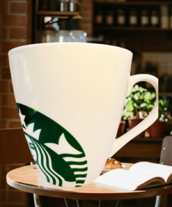 Starbucks White Giant Siren Mug displayed in a warm café with an open book