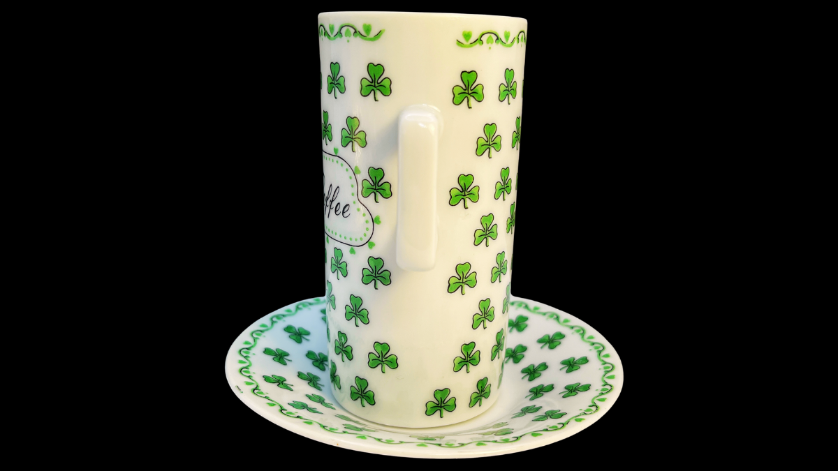 Front view of a tall ceramic Irish Coffee cup and saucer set decorated with repeating green shamrocks and a central panel reading “Irish Coffee” in script lettering.