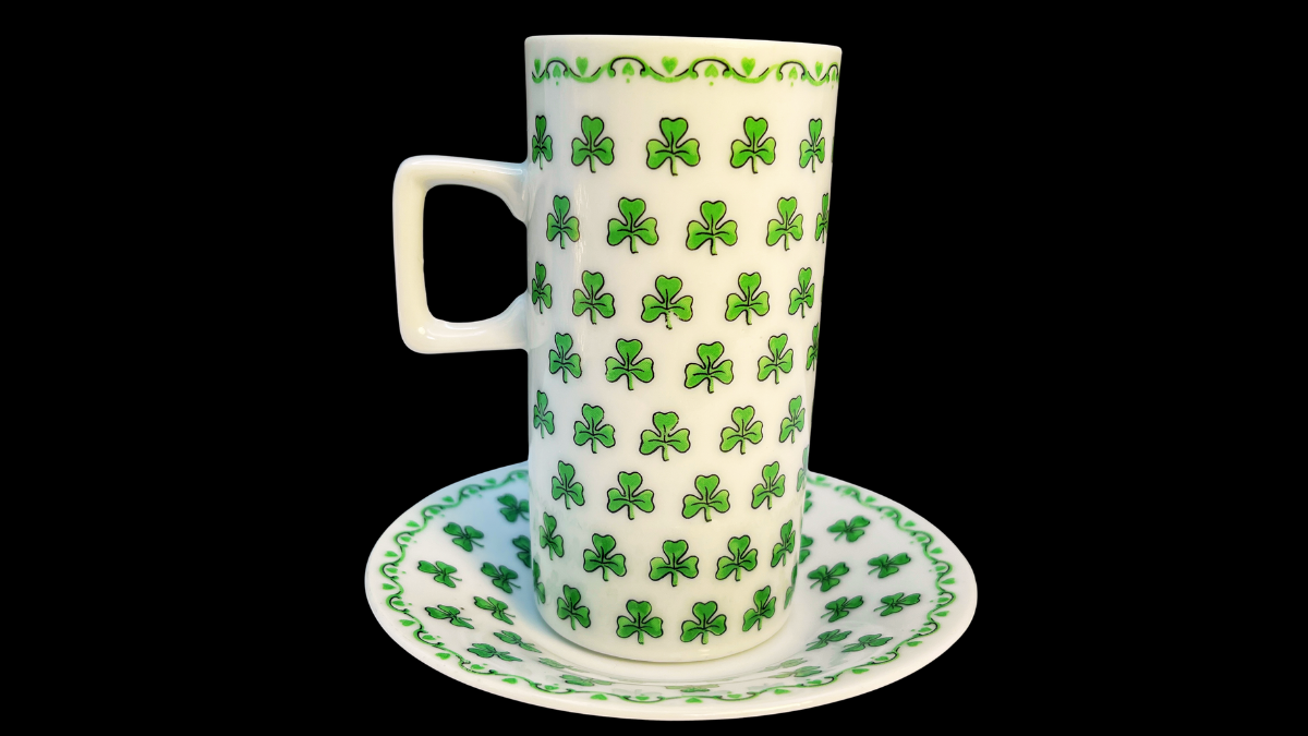 Side middle view of the tall Irish Coffee cup highlighting the dense repeating shamrock pattern that covers the ceramic surface along with the decorative green border near the rim.