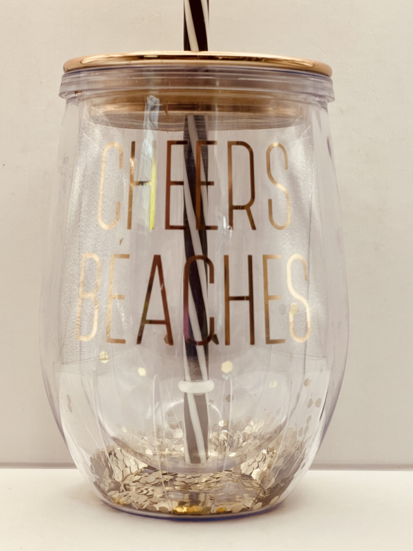 The  Cheers Beaches Glitter Stemless Tumbler features a unique double-walled design. With a clear outer wall showcasing the playful gold lettering “CHEERS BEACHES.”