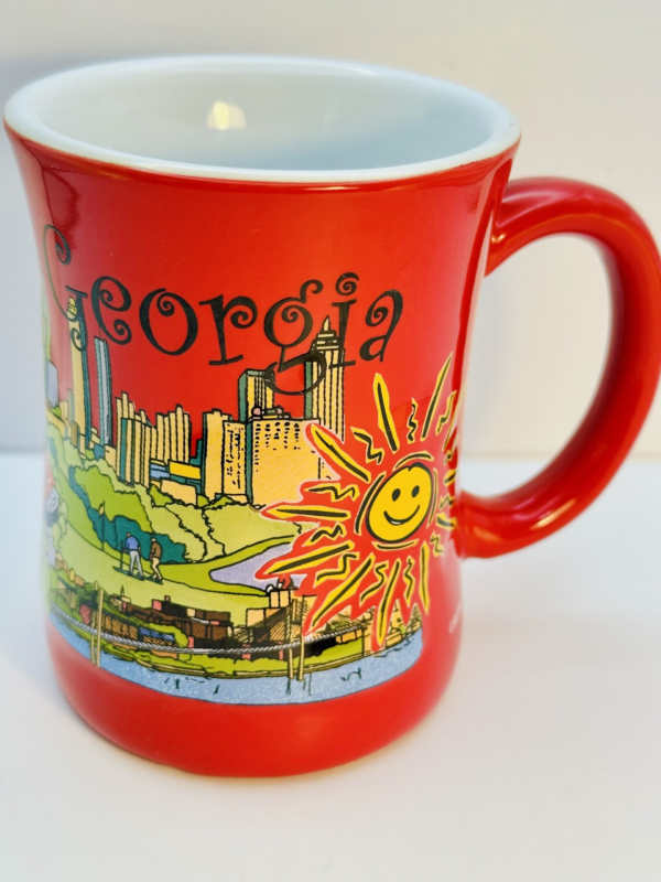 The Smiling Sun Georgia Skyline Souvenir Mug features a vibrant cartoon-style design showcasing a charming city skyline, a flowing river,. And, of course, a smiling sun that beams as brightly as Georgia hospitality.

In fact, its crafted from durable ceramic with a 12-ounce capacity. This souvenir coffee cup is perfect for anyone who loves to sip with style and a story.