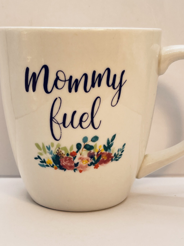 Introducing the Mommy Fuel White Floral Mug. It’s the perfect #cupofmood and your new favorite way to sip, survive, and slay the day. Because motherhood runs on hugs, chaos… and caffeine. Lots of it.

Indeed, this 20-ounce ceramic beauty is here to say what every mom is thinking (and definitely feeling). Fueled by coffee, sustained by chaos. The words “Mommy Fuel” are boldly printed in big black letters on the front. Making it crystal clear what’s in her cup—and why it’s sacred.