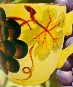 Tabletops Unlimited Vino Hand Painted Grape Mug displayed beside vineyard grapes
