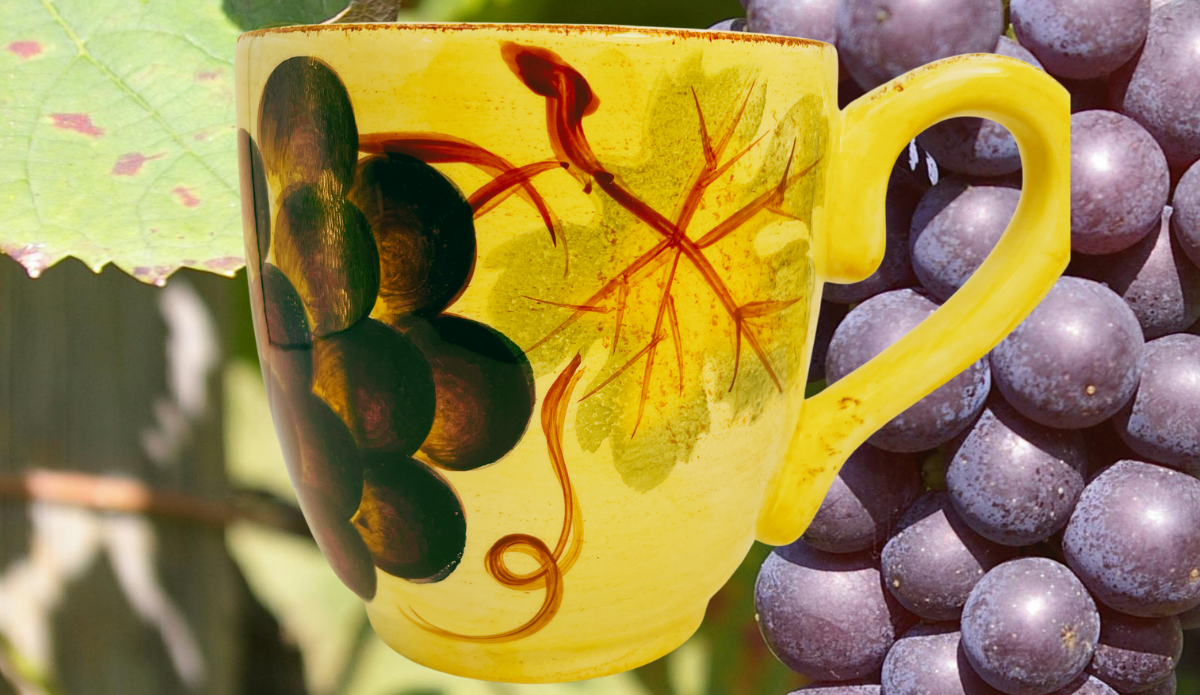 Tabletops Unlimited Vino Hand Painted Grape Mug displayed beside vineyard grapes