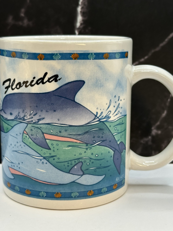 Dive into a tropical paradise with the Dolphins Florida Souvenir Mug. It’s the perfect #cupofmood to bring the magic of Florida’s coastlines into your daily routine.Indeed, this 8-ounce white ceramic mug is adorned with beautiful dolphins gracefully swimming through the water, wrapping around the entire outside of the mug.Whether you’re sipping your morning coffee, enjoying an afternoon tea, or savoring a hot cocoa on a chilly evening. This mug will make every sip feel like a getaway to the sunshine state.