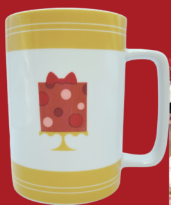 Cake Boss Yellow Mini Cakes Porcelain Mug displayed in a cozy bakery kitchen with coffee and baked treats