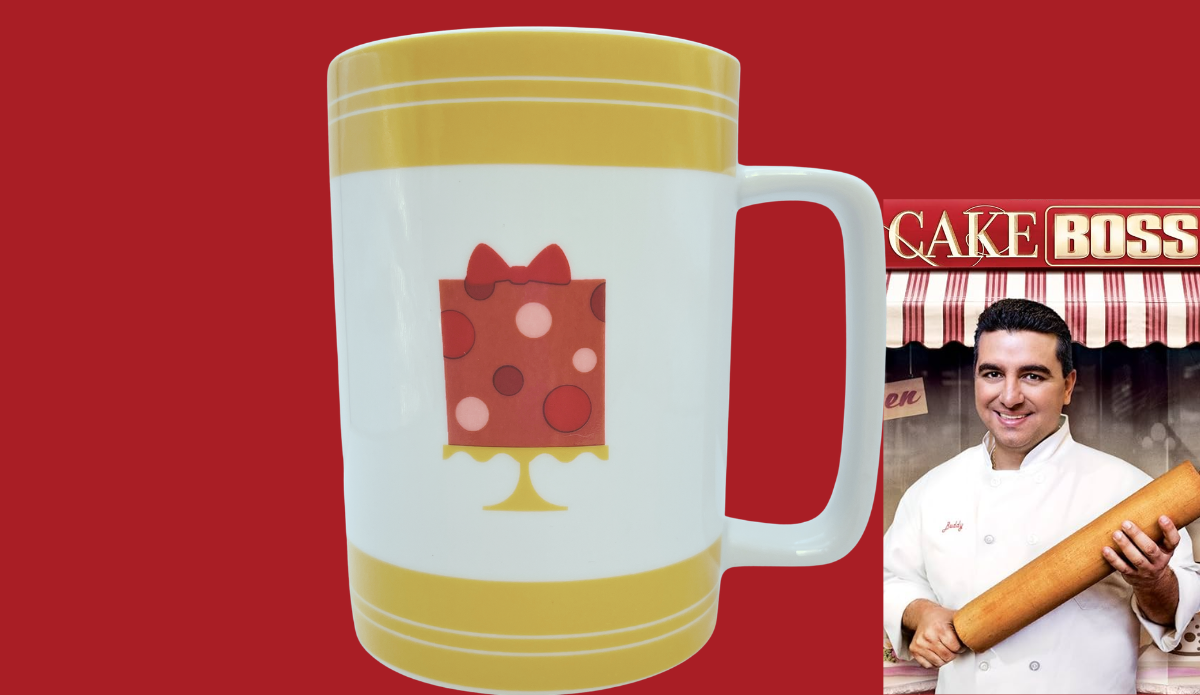 Cake Boss Yellow Mini Cakes Porcelain Mug displayed in a cozy bakery kitchen with coffee and baked treats