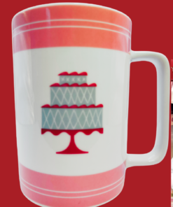 Cake Boss Pink Mini Cakes Porcelain Mug displayed in a cozy bakery kitchen with coffee and desserts