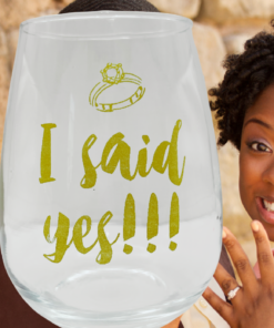 I Said Yes Stemless Wine Glass displayed with smiling newly engaged woman showing ring