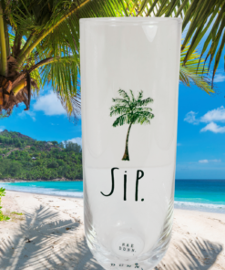 Rae Dunn SIP champagne flute displayed on a tropical beach with palm trees and turquoise ocean