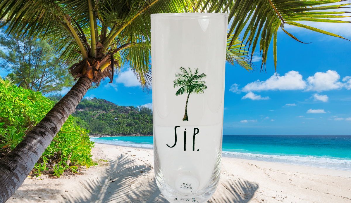 Rae Dunn SIP champagne flute displayed on a tropical beach with palm trees and turquoise ocean
