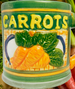 Vintage 3D Carrots Mug displayed with fresh carrots, leafy carrot tops, raised vegetable artwork, and sculpted carrot handle.