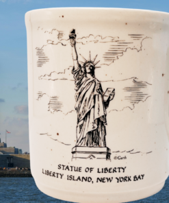 Statue of Liberty Speckled Mug displayed beside Liberty Island and the Statue of Liberty under a blue sky
