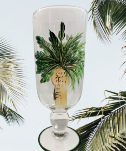 Florida Marketplace Palm Island Hand Painted Glass Goblet displayed among tropical palm fronds outdoors